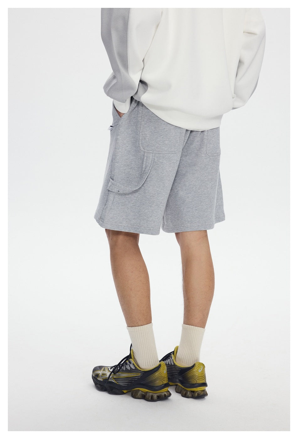 Rear three-quarter view of a model wearing light gray shorts with large patch pockets and a side utility loop.