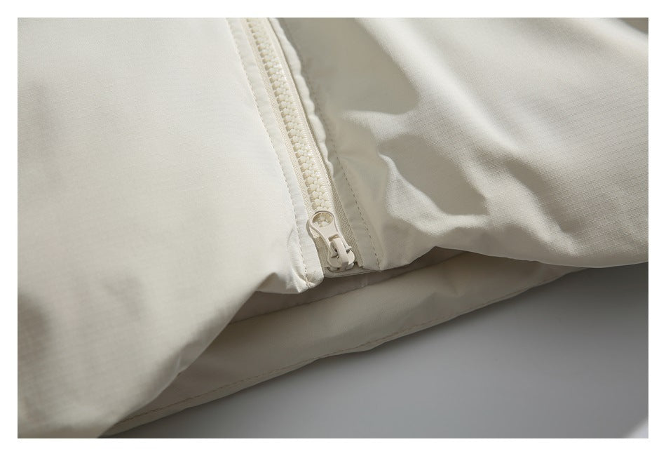 Close-up of the lower end of an off-white jacket's front zipper.