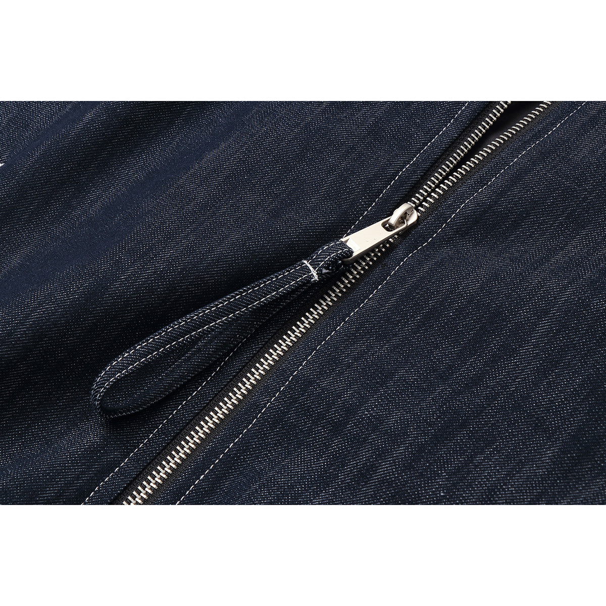 Close-up of the jacket's silver zipper and long fabric pull against dark indigo material.