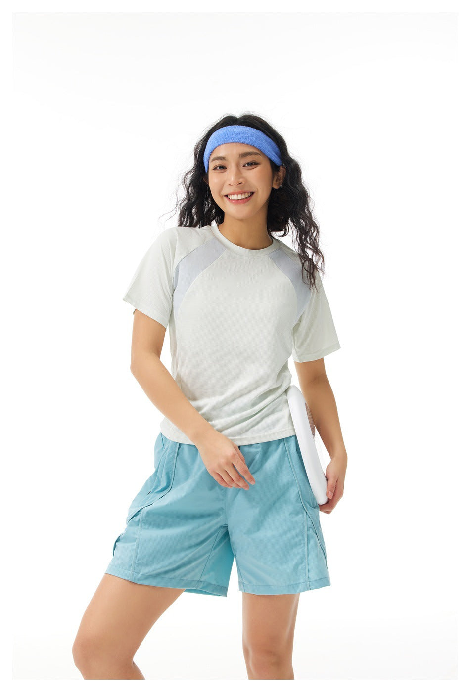 Model wearing a white short-sleeve athletic top with pale gray shoulder panels and turquoise shorts.