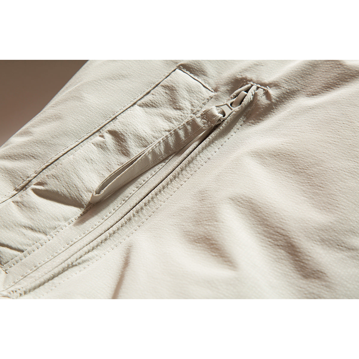 Close-up of an off-white jacket's zippered pocket and visible stitching.