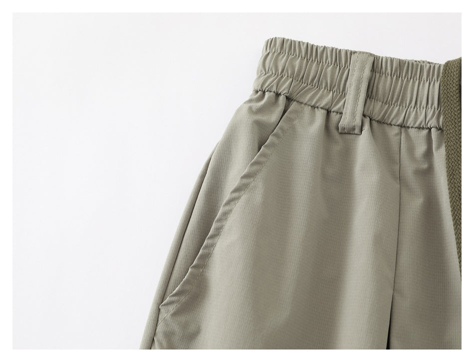Close-up of light gray-green shorts showing the gathered elastic waistband, belt loop, and side pocket seam.