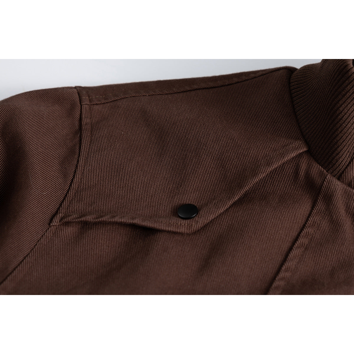 Close-up of a brown jacket’s shoulder flap with a black snap button.