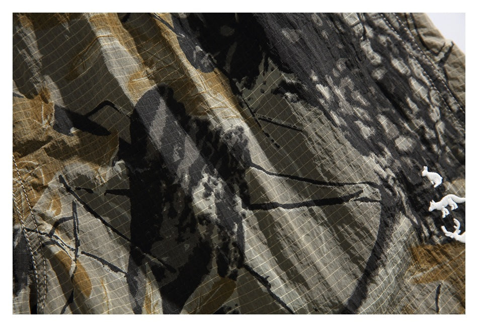 Close-up of the shorts' brown, green, and black camouflage print with part of the white embroidery visible.