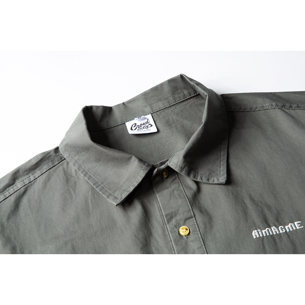 Close-up of a gray-green short-sleeve button-up shirt collar, buttons, and white chest embroidery.