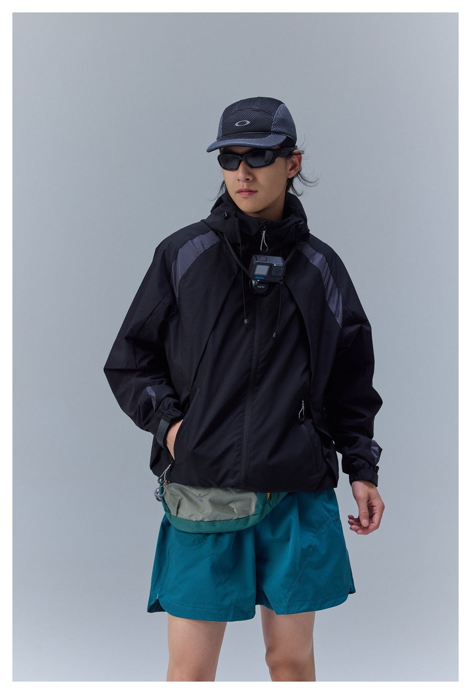 Closer view of a model wearing a black hooded jacket with gray shoulder panels and teal shorts.