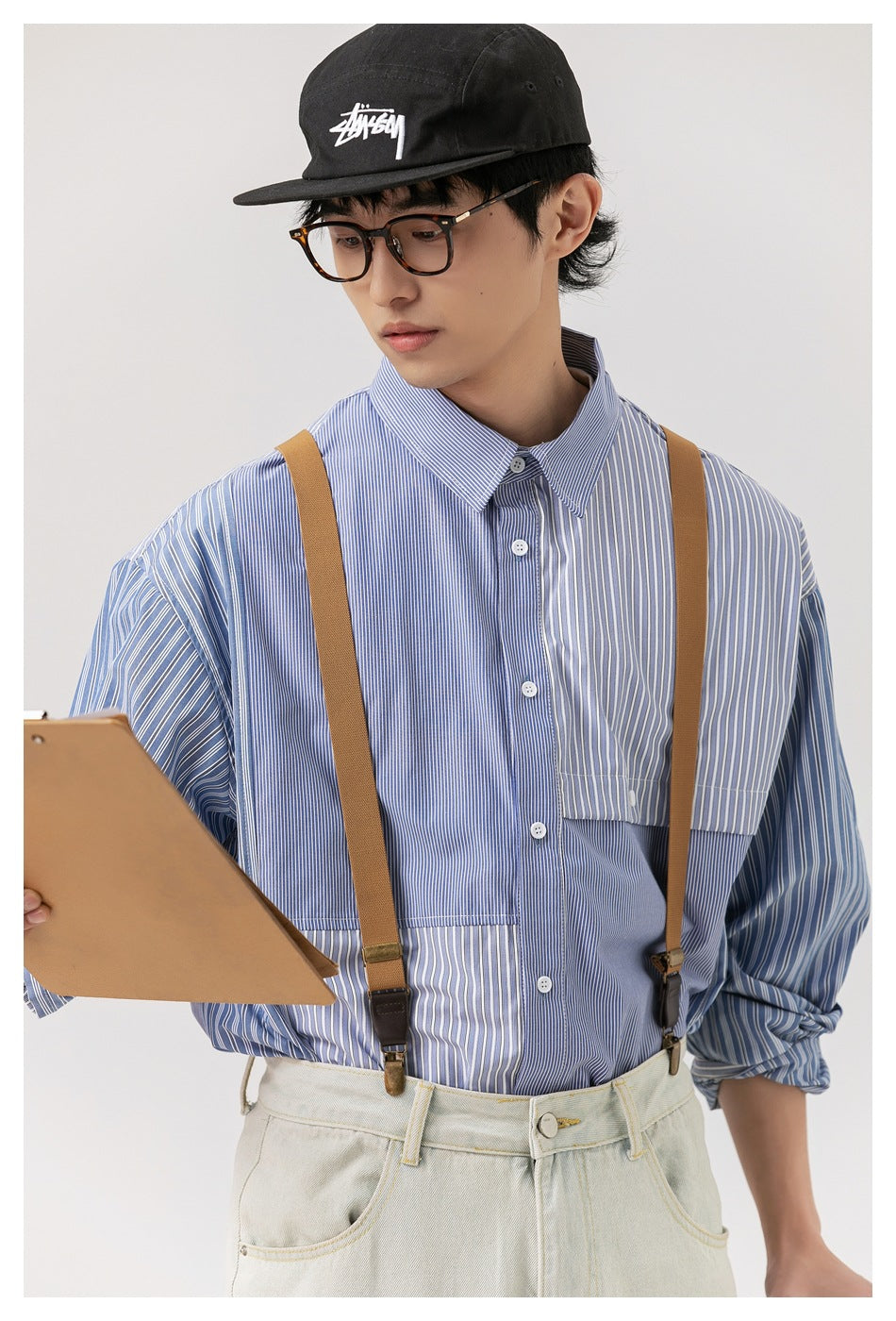 Model wearing a blue patchwork striped button-up shirt with a pointed collar and chest pocket.
