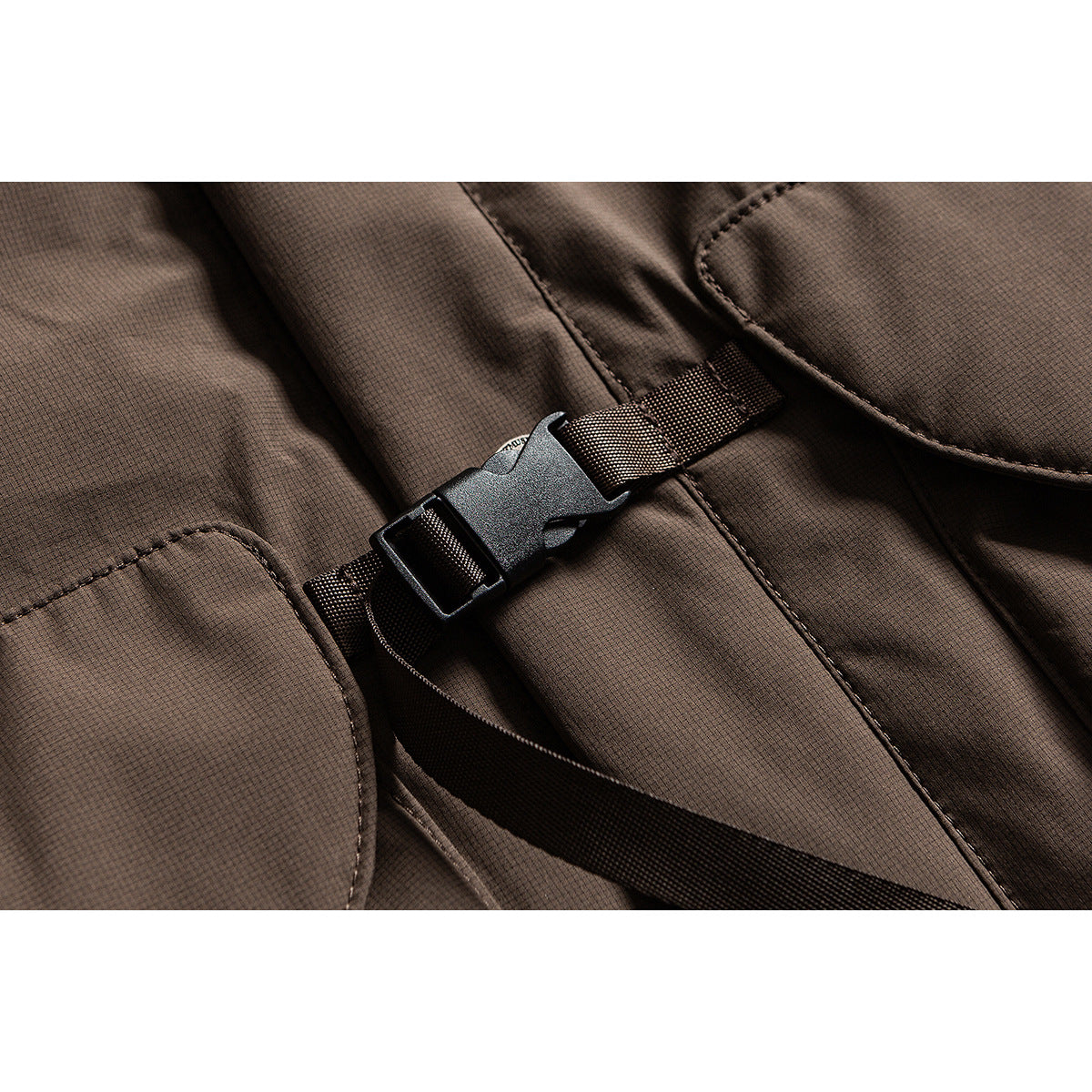 Close-up of a brown jacket with a black adjustable buckle strap and stitched pocket edges.