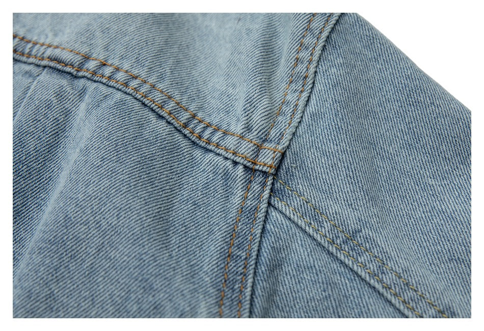 Close-up of light blue denim jacket fabric with intersecting seams and tan stitching.