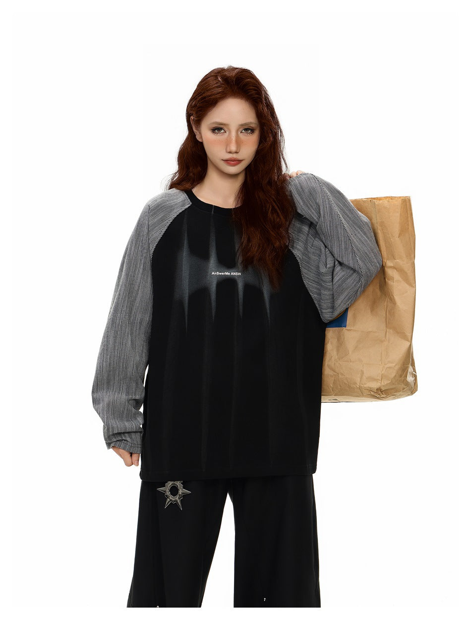 Model wearing an oversized black top with gray pinstriped raglan sleeves and small white chest lettering, paired with wide