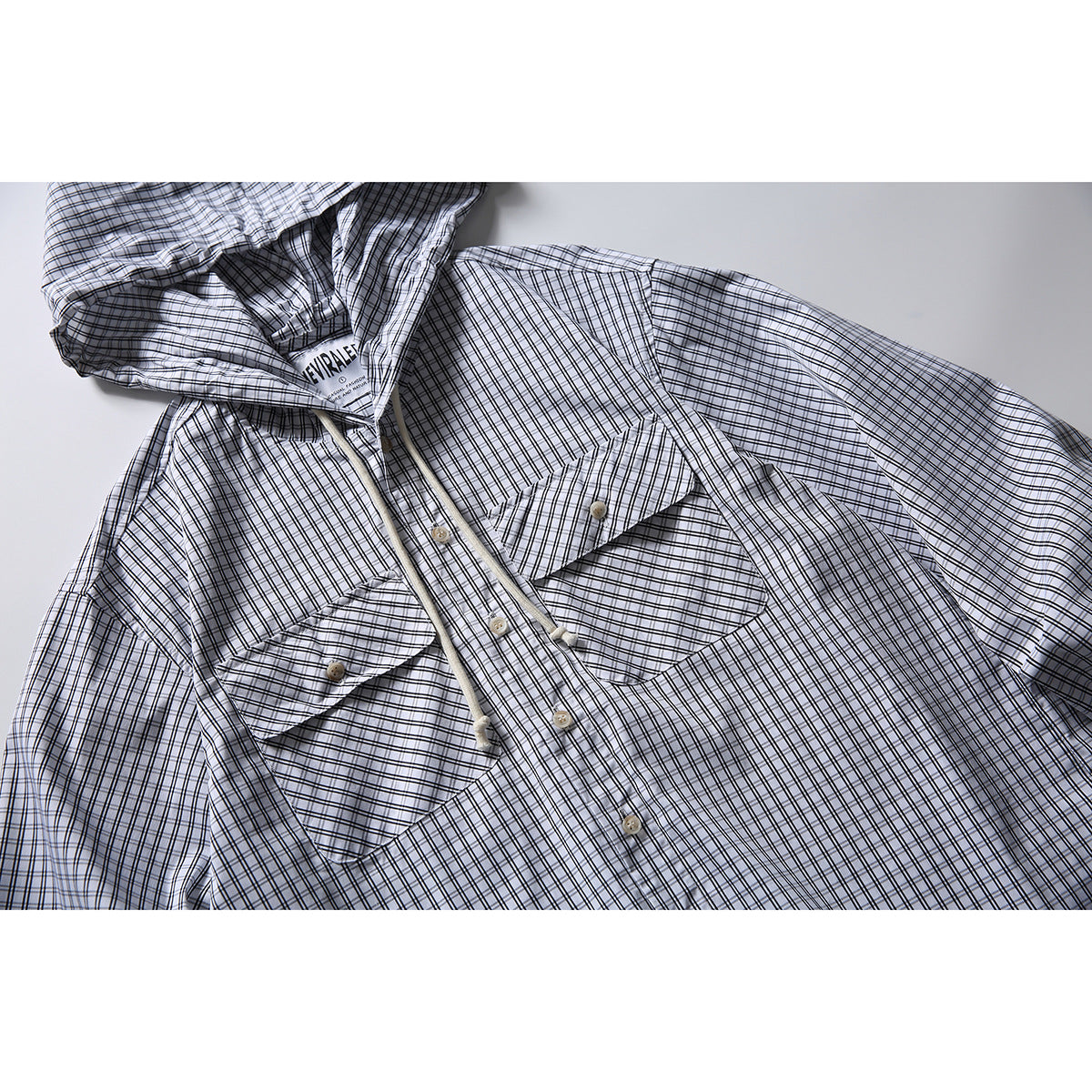 Close-up of a white shirt with black windowpane checks, buttoned chest pockets, front buttons and a drawstring hood.