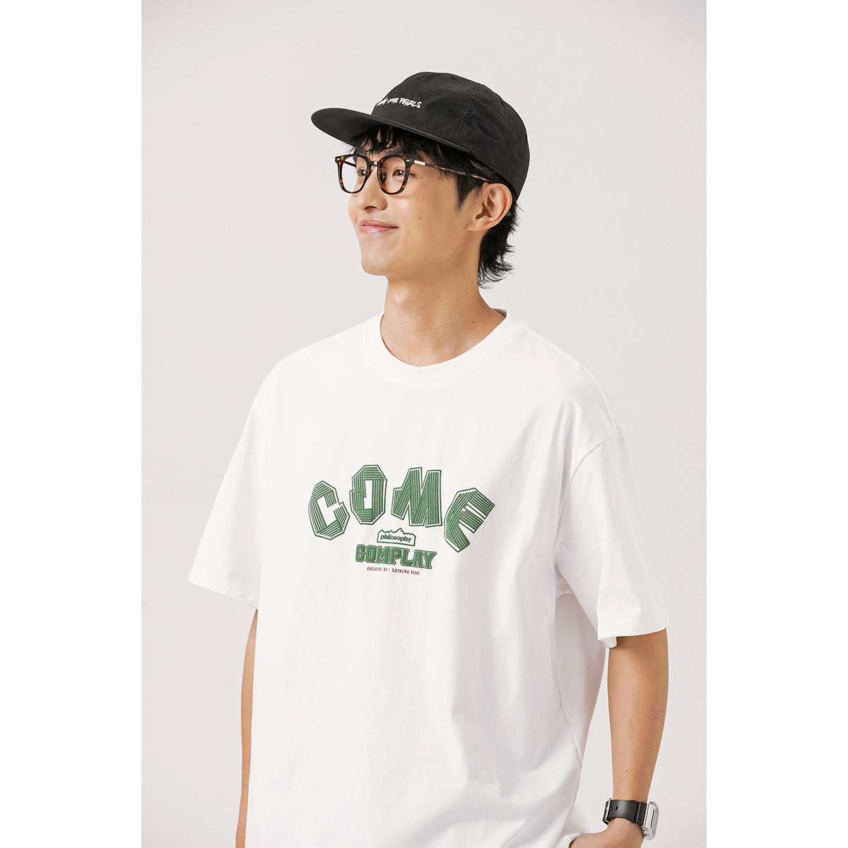 Model wearing a white T-shirt with a large dark-green graphic across the chest.
