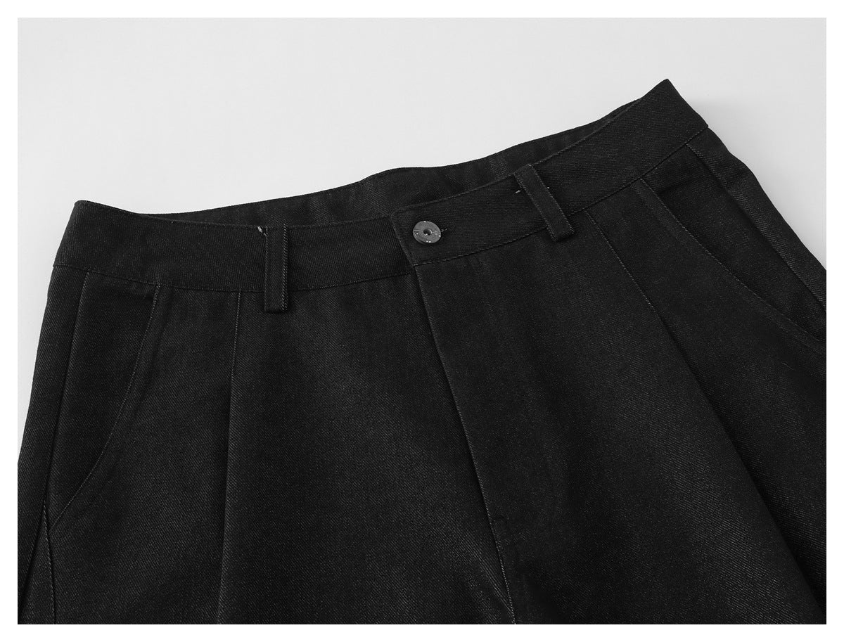 Close-up of black shorts showing the front waistband, button, belt loops, and pleated front.