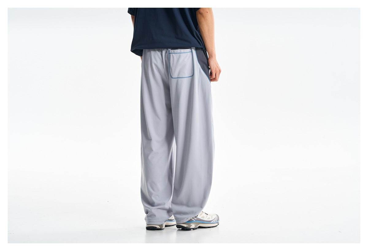 Back view of a model wearing loose light gray pants with blue-trimmed rear pocket and side piping.
