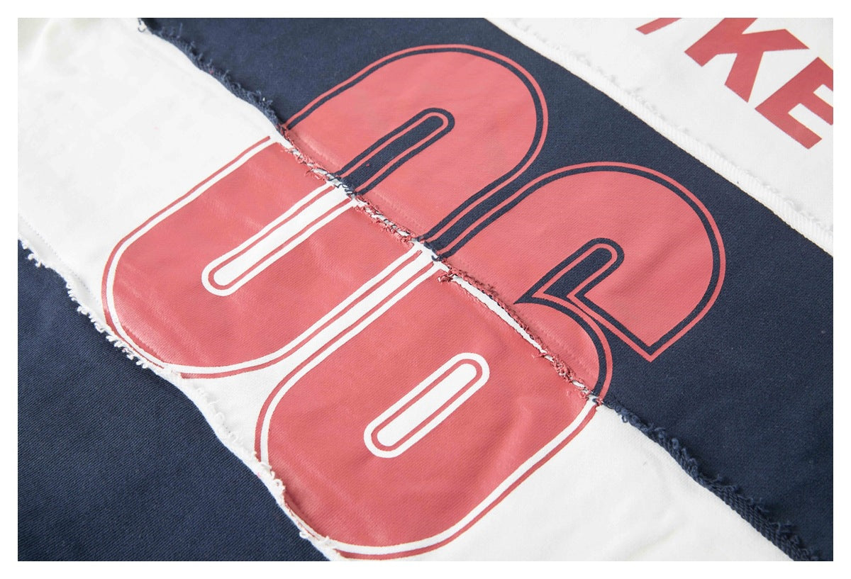 Close-up of oversized coral-red outlined lettering across navy and white garment panels.