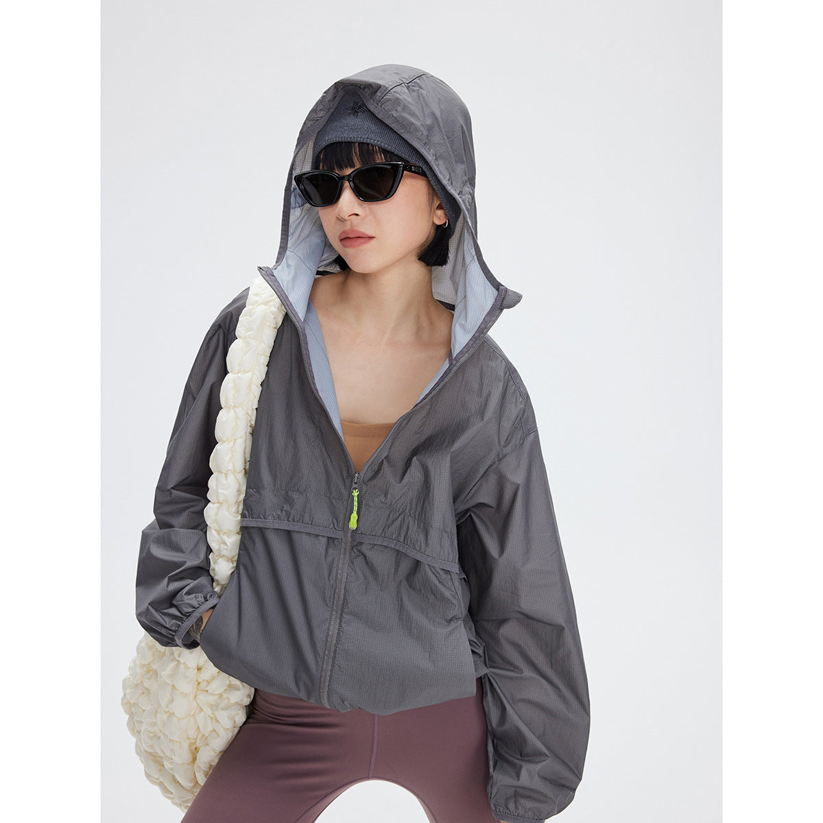 Model wearing a charcoal gray hooded zip jacket with a bright green zipper pull.