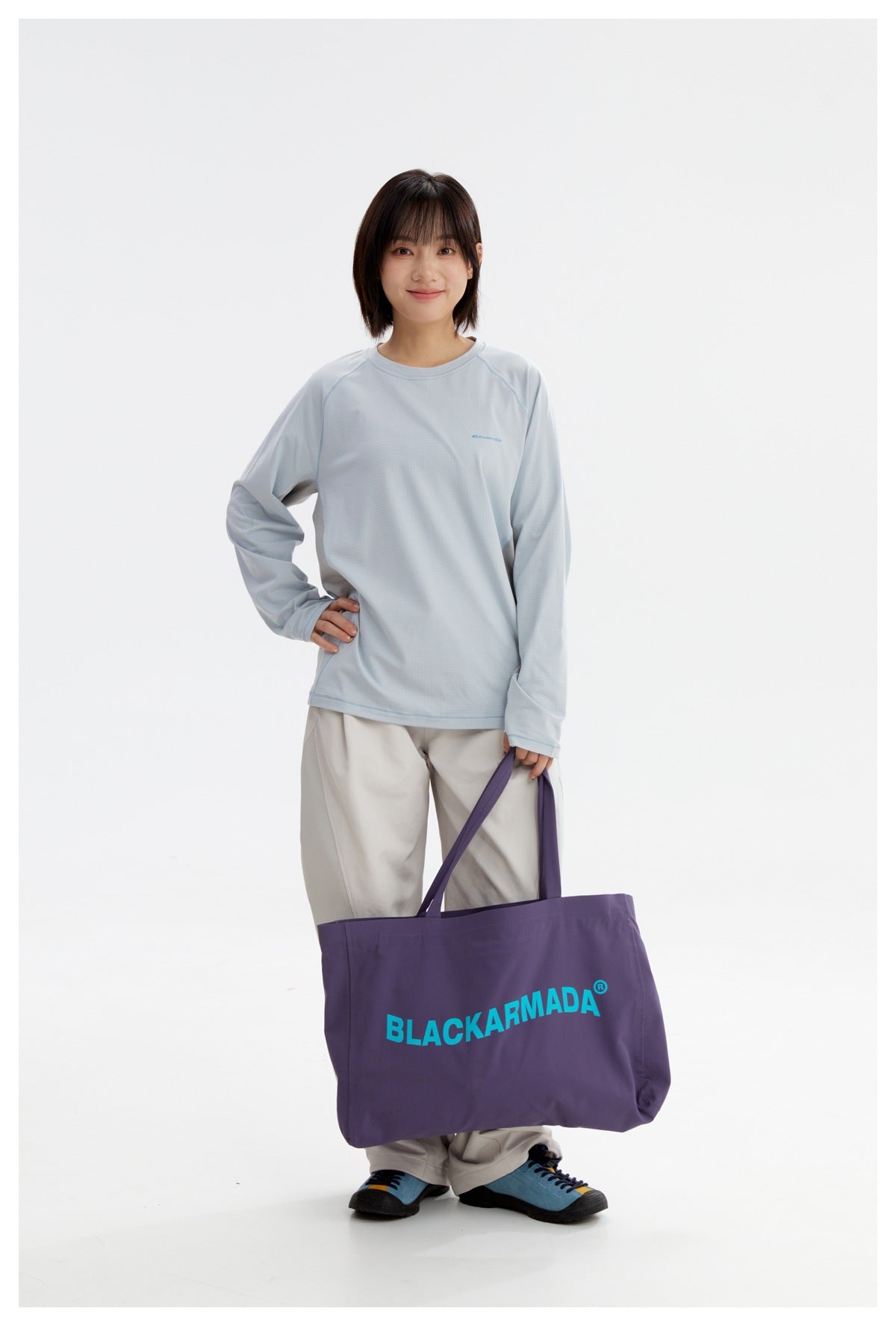 Person wearing the frost blue long-sleeve top with light gray wide pants, holding a large purple tote bag