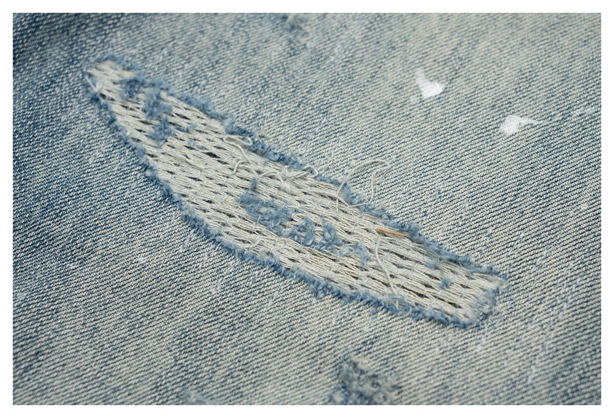 Close-up of a frayed, woven repair detail on faded blue denim.