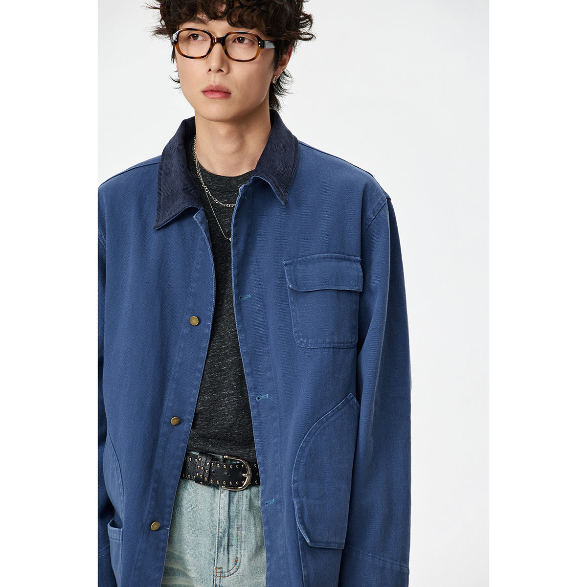 Close view of a model wearing a blue work jacket with a dark collar, brass-tone buttons and large pockets.
