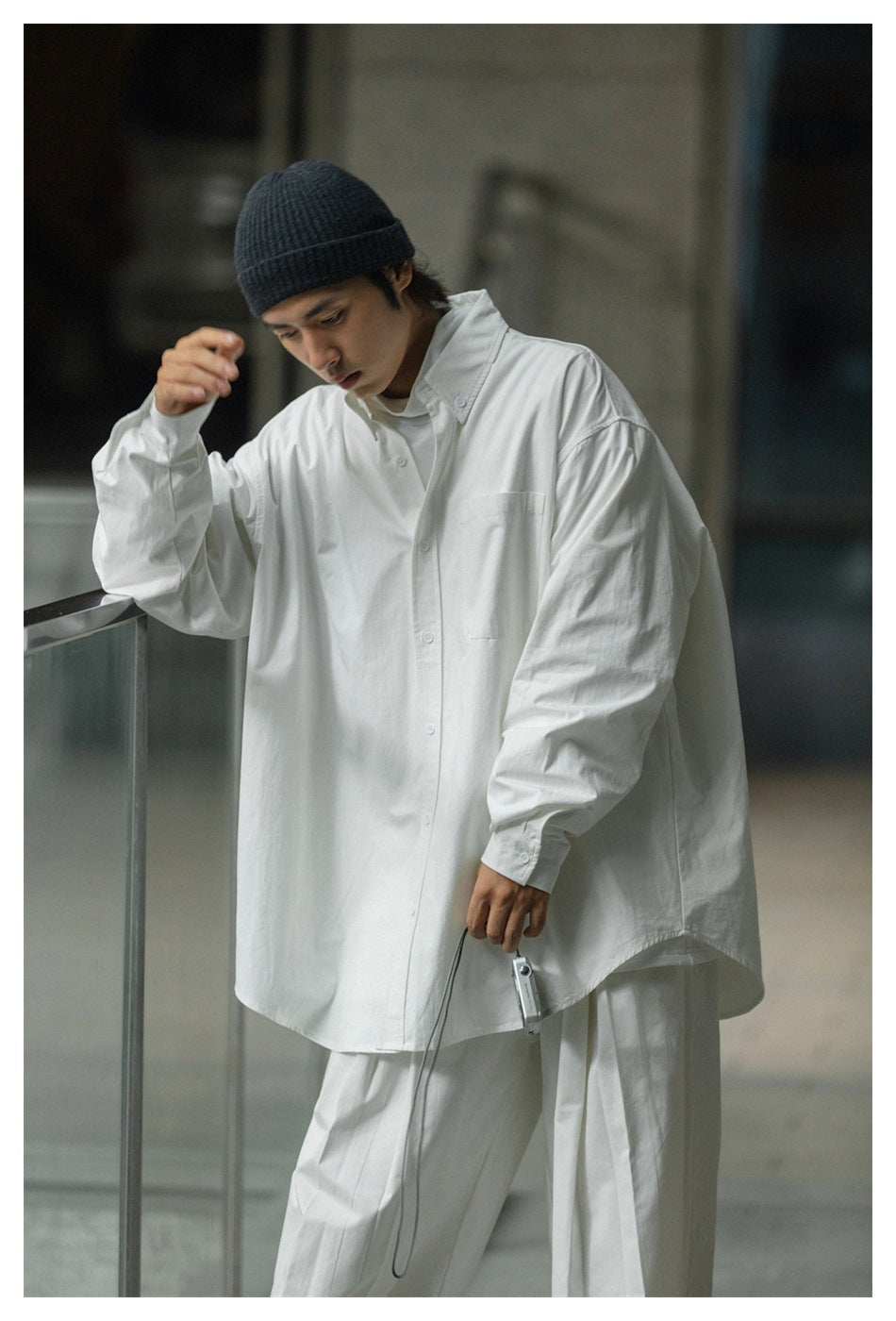 Model wearing an oversized white button-up shirt with a chest pocket and white trousers.