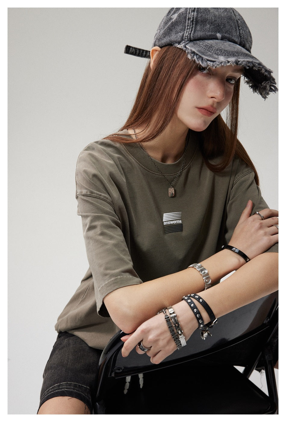 Close view of a model in an olive-gray oversized T-shirt with a small striped chest graphic.