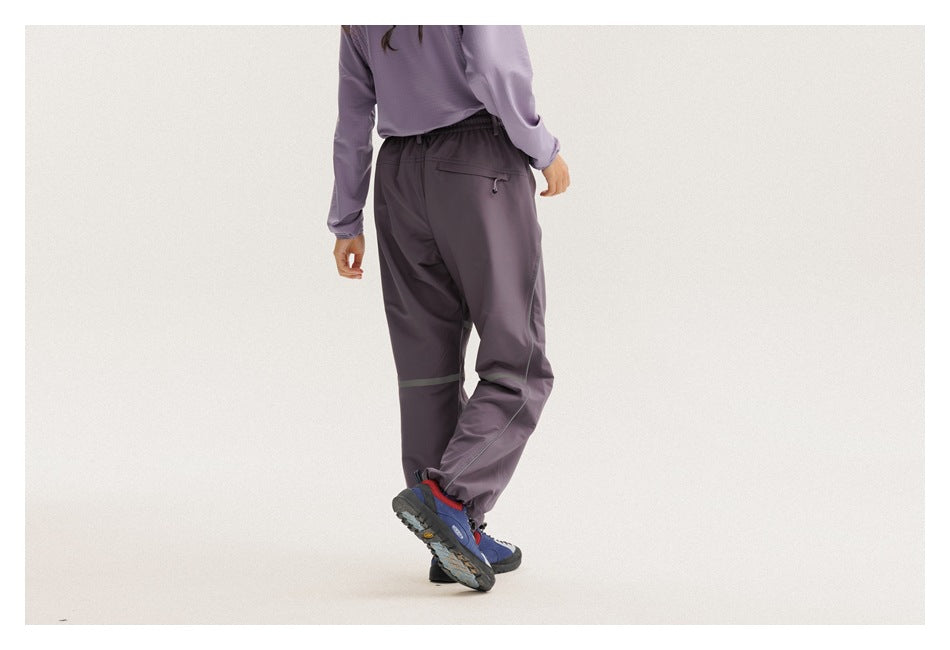 Three-quarter rear view of a model in loose charcoal-purple pants with muted reflective bands and an elastic waist.