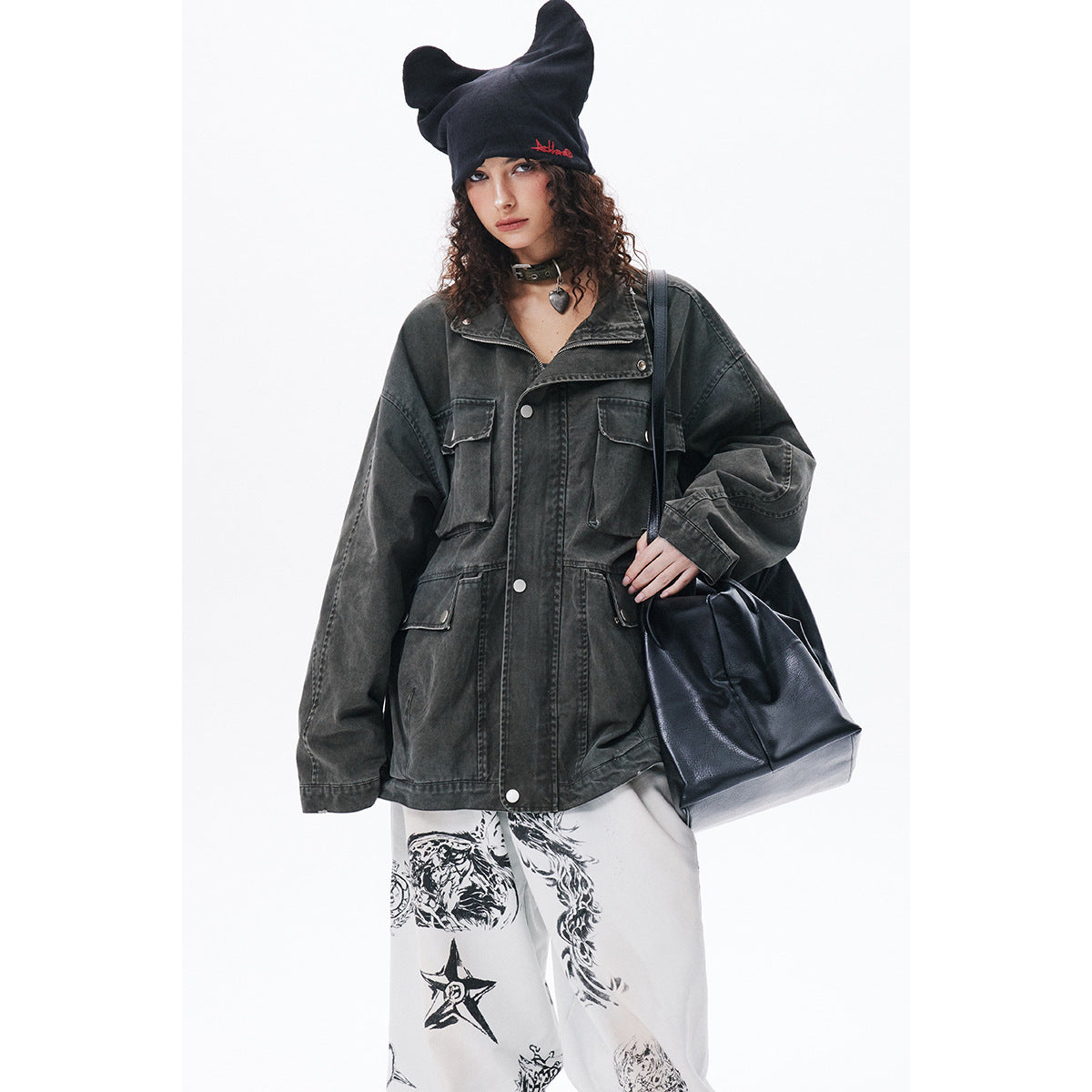 Model in a charcoal oversized utility jacket and white graphic pants, shown with a black beanie and tote bag.
