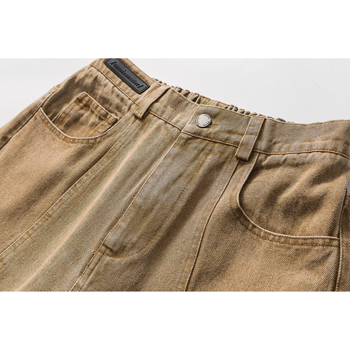 Close-up of tan washed jeans showing the waistband, button, belt loops, and front pockets.