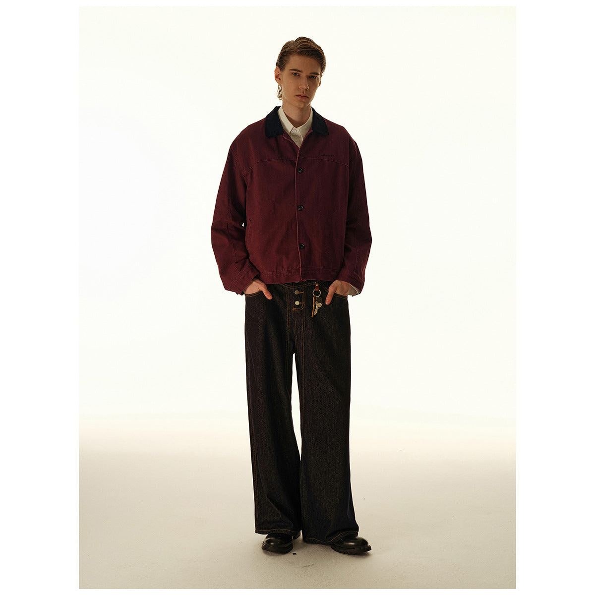 Model wearing a burgundy button-front jacket with a dark collar and dark wide-leg jeans, front view.
