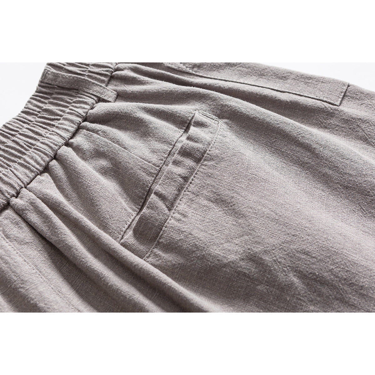 Close-up of light gray shorts showing the gathered waistband, stitching, and pocket area.