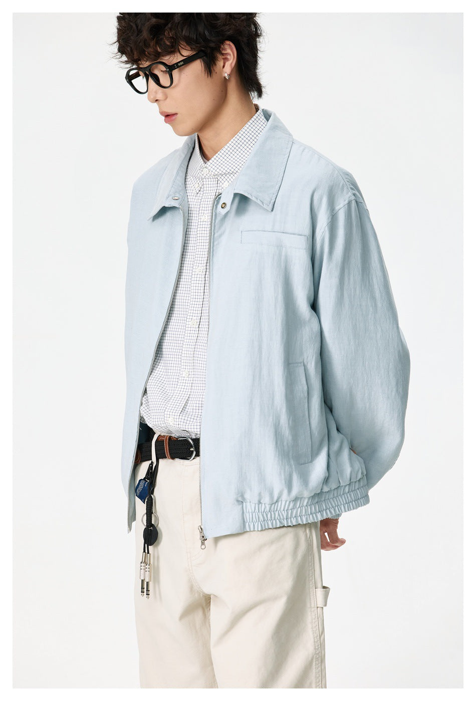 Model wearing a pale blue zip-front jacket with a wide collar, chest pocket and elasticated hem over a checked shirt.