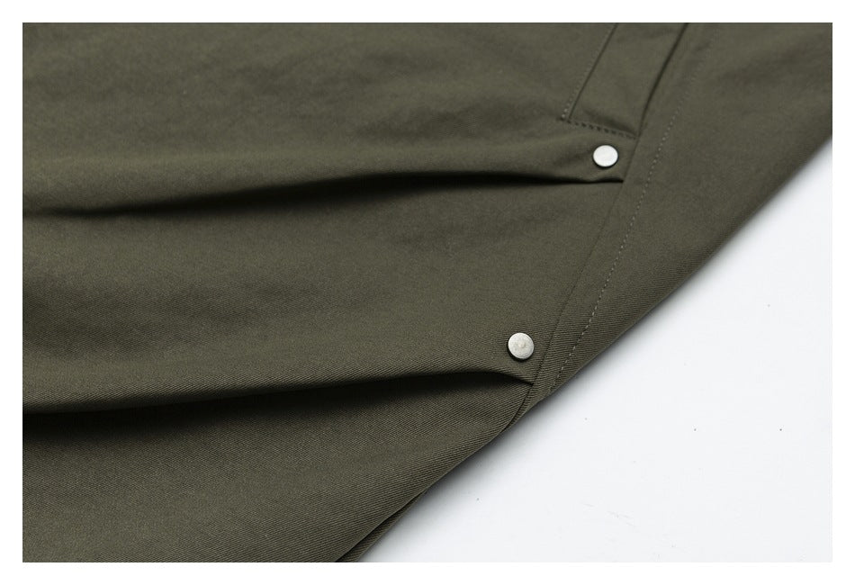 Close view of olive trouser fabric with seams and two round silver-tone rivets.