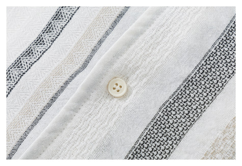 Close-up of a cream button and textured white fabric with black and beige woven stripes.