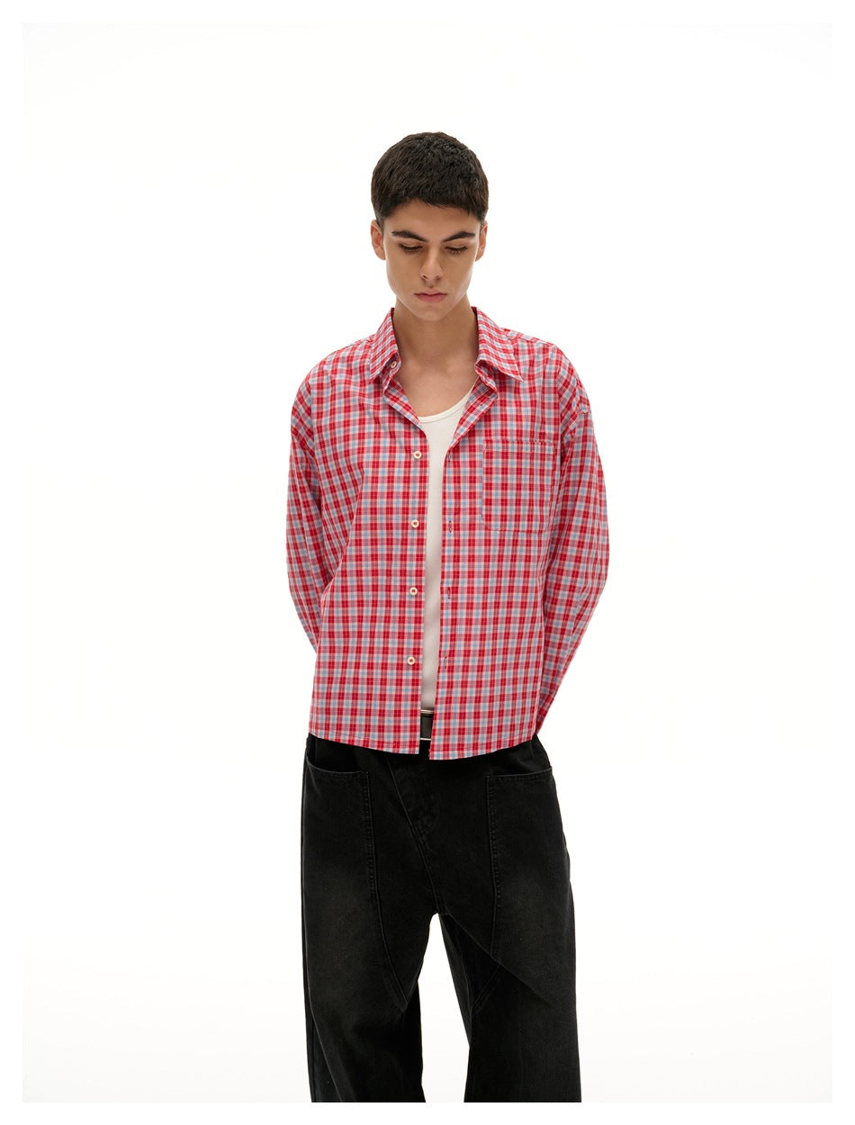 Model wearing an open red-and-white plaid button-up shirt over a white top with black trousers.