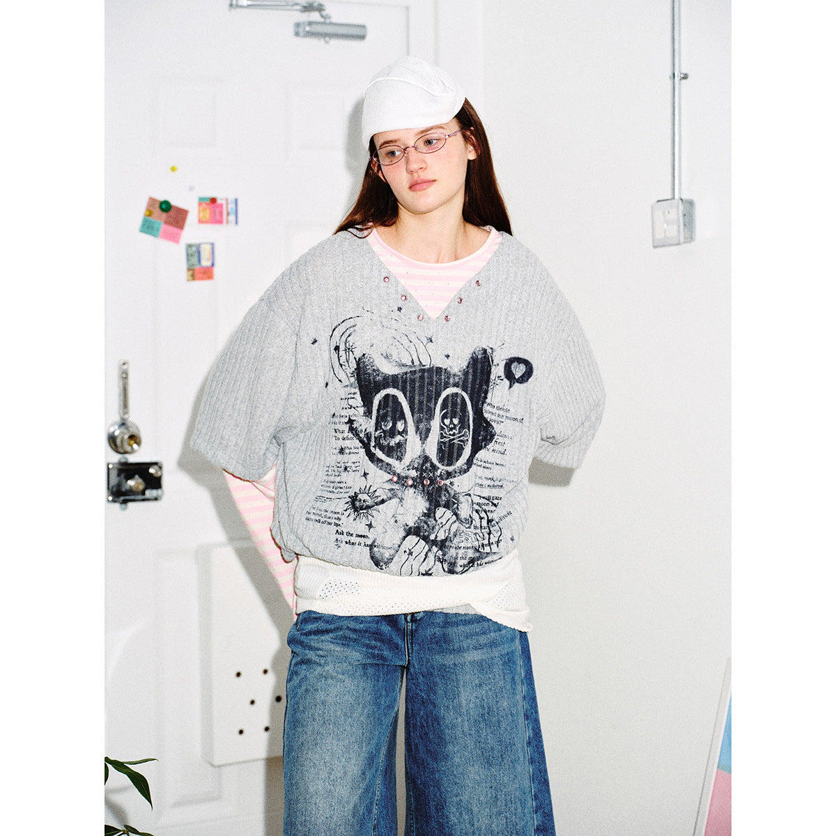Model wearing a gray graphic V-neck top over pink stripes with blue denim culottes, shown from the front.