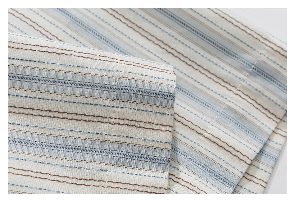 Close-up of a folded edge and stitching on cream fabric with fine blue and brown stripes.