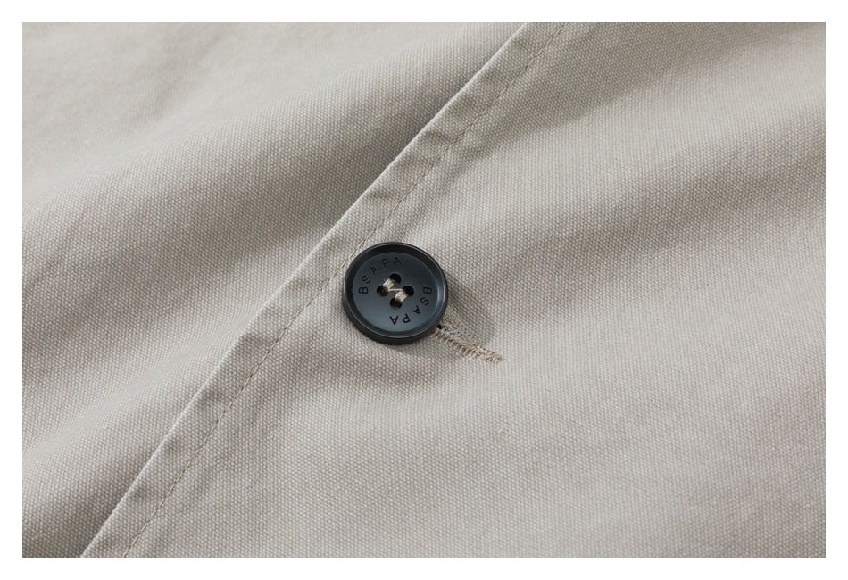 Close-up of a dark four-hole button marked BSAPA on beige woven fabric.