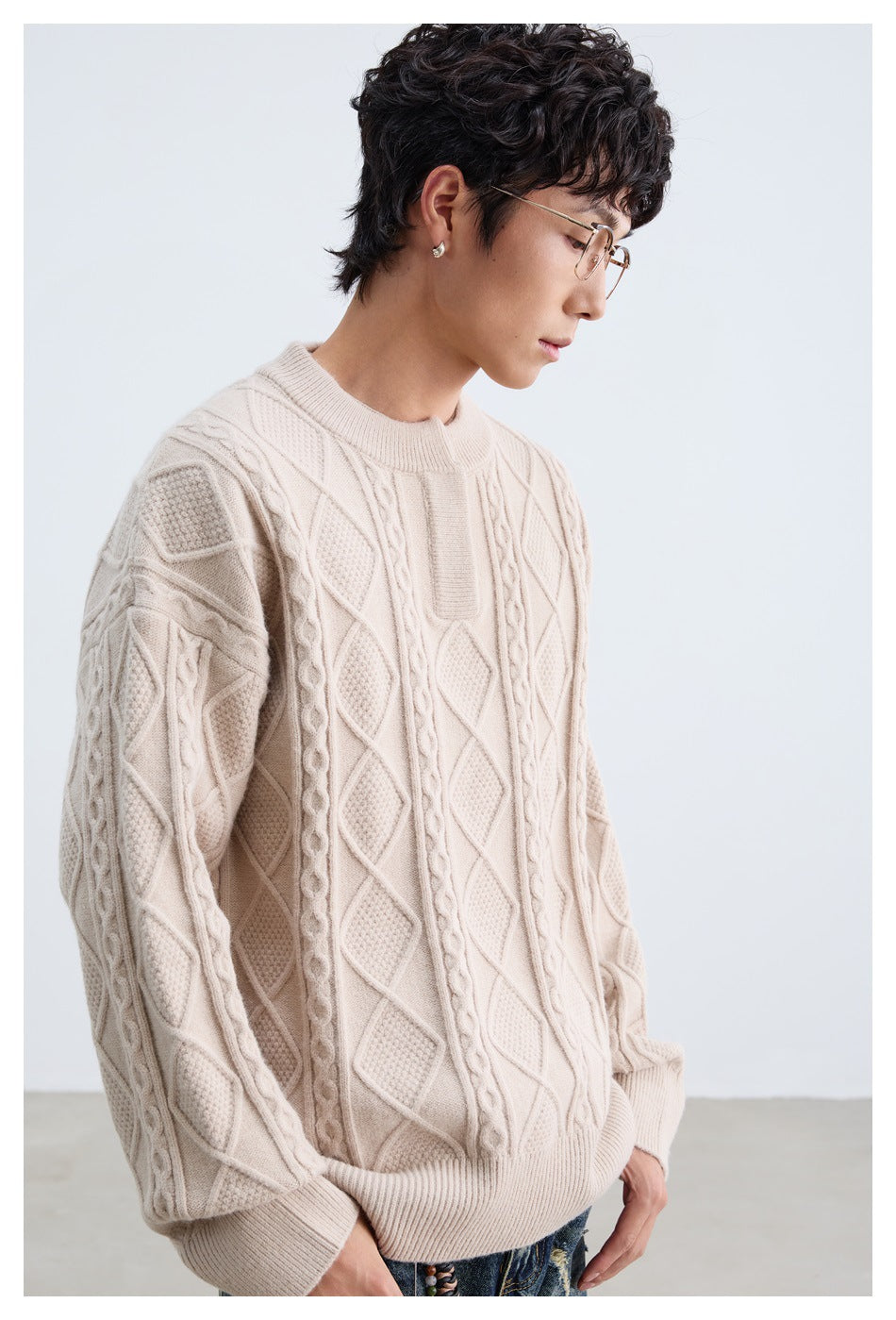 Side view of a model wearing a cream cable-knit sweater with raised diamond and braided patterns.