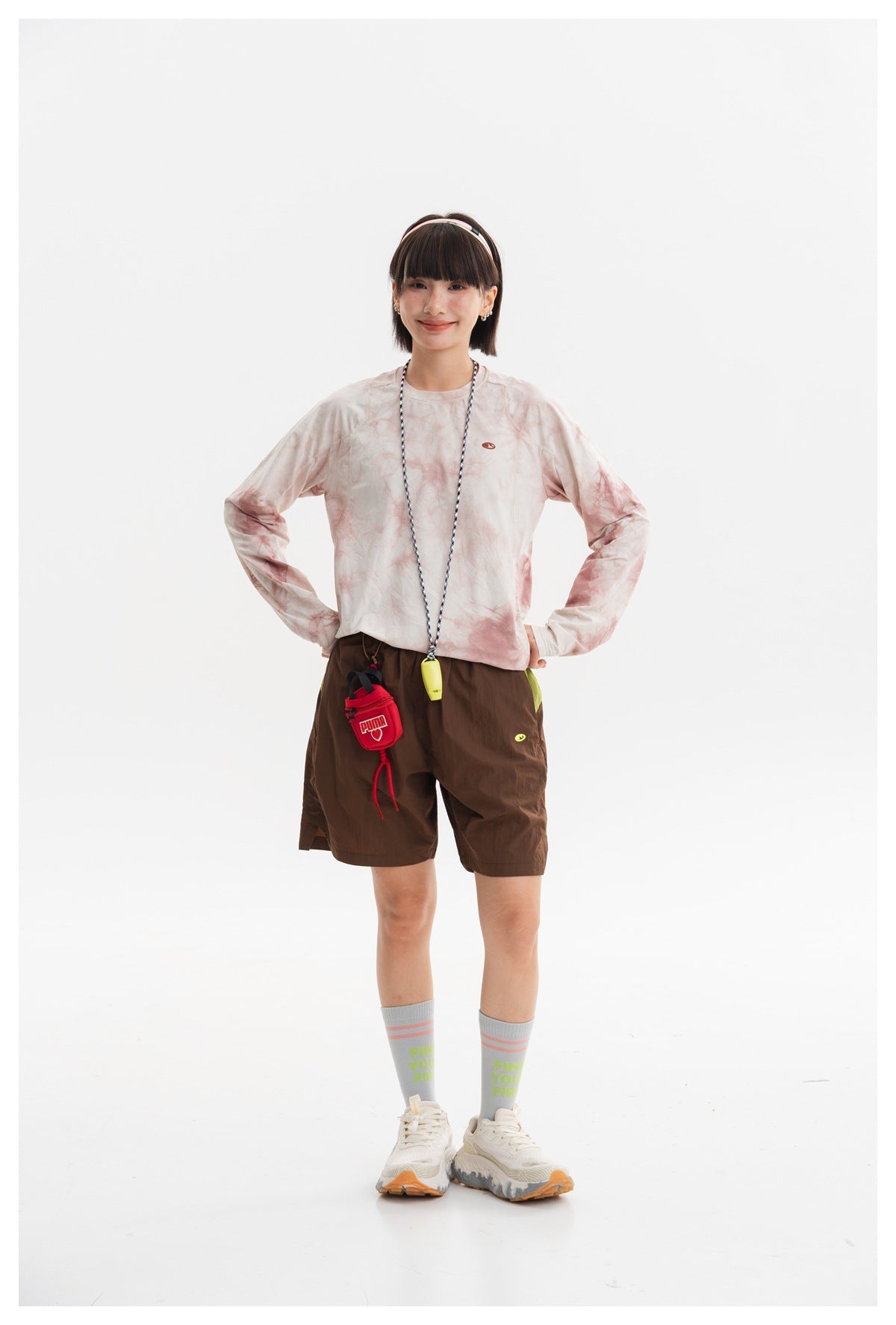 Model posing in a cream and dusty-pink tie-dye long-sleeve crewneck shirt and brown shorts, front view.