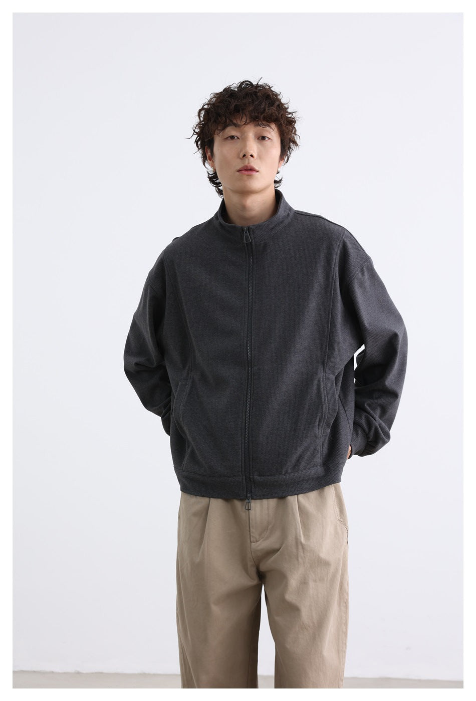 Model wearing dark gray zip jacket with khaki trousers, front view with hand in pocket