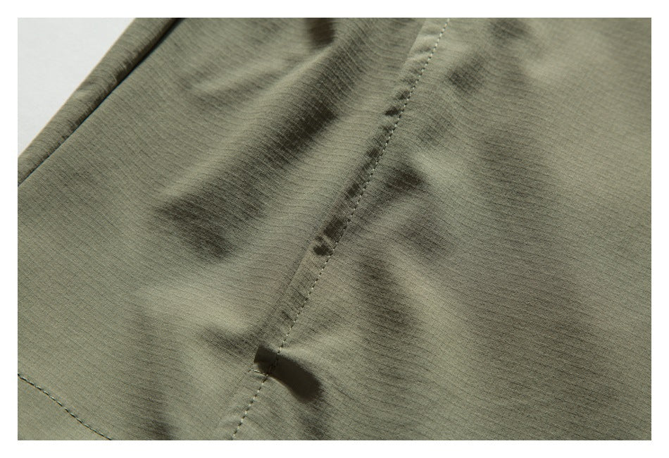 Close-up of olive khaki garment fabric with a stitched seam and small fabric tab.