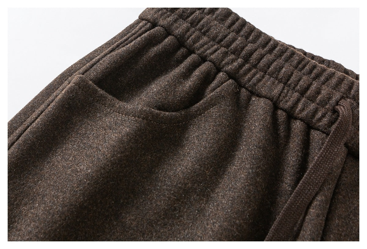 Close-up of dark brown pants showing the elastic waistband, slanted pocket opening and drawcord.