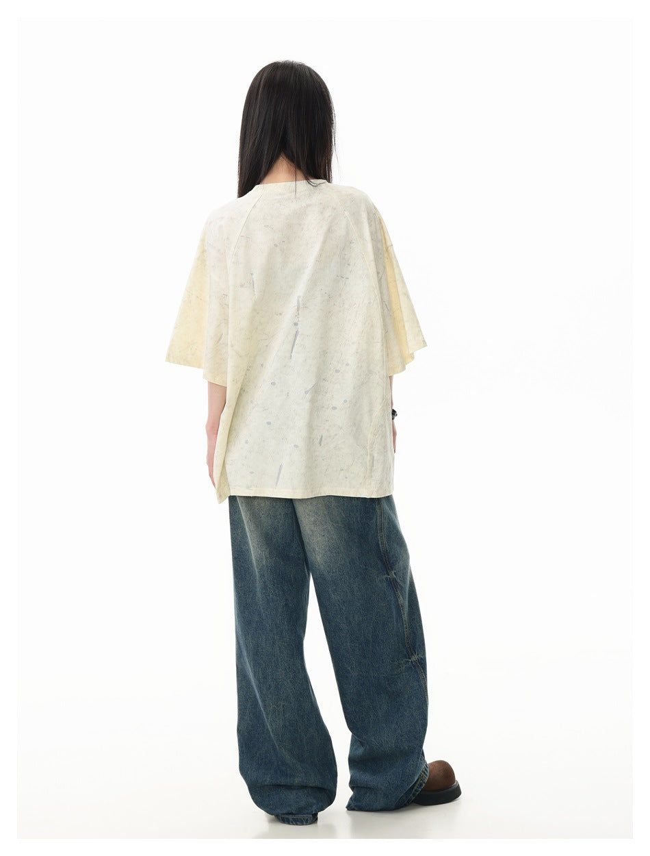 Back view of a model wearing an oversized ivory, gray-speckled T-shirt with loose dark blue jeans.