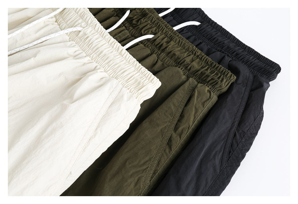 Close view of cream, olive green, and black drawstring pants arranged side by side.
