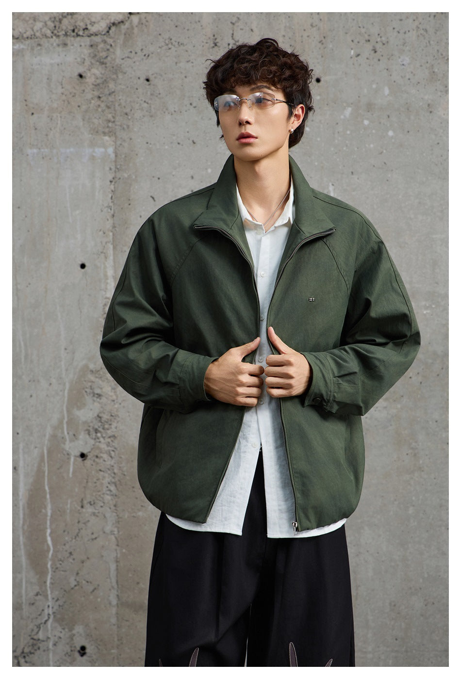 Front view of a person wearing an olive-green zip jacket with a raised collar and small chest detail.
