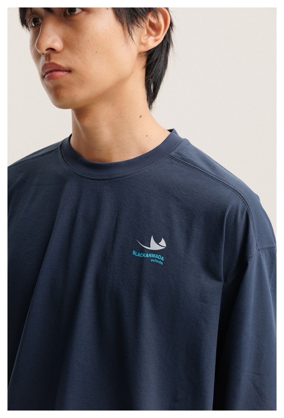 Close-up of a navy long-sleeve shirt showing its crew neck, shoulder seams, and white-and-turquoise chest emblem.