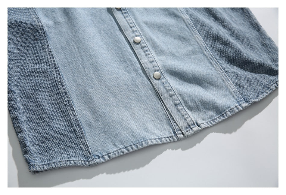 Cropped view of a light blue denim button-front garment with darker patterned side panels and a stitched hem.