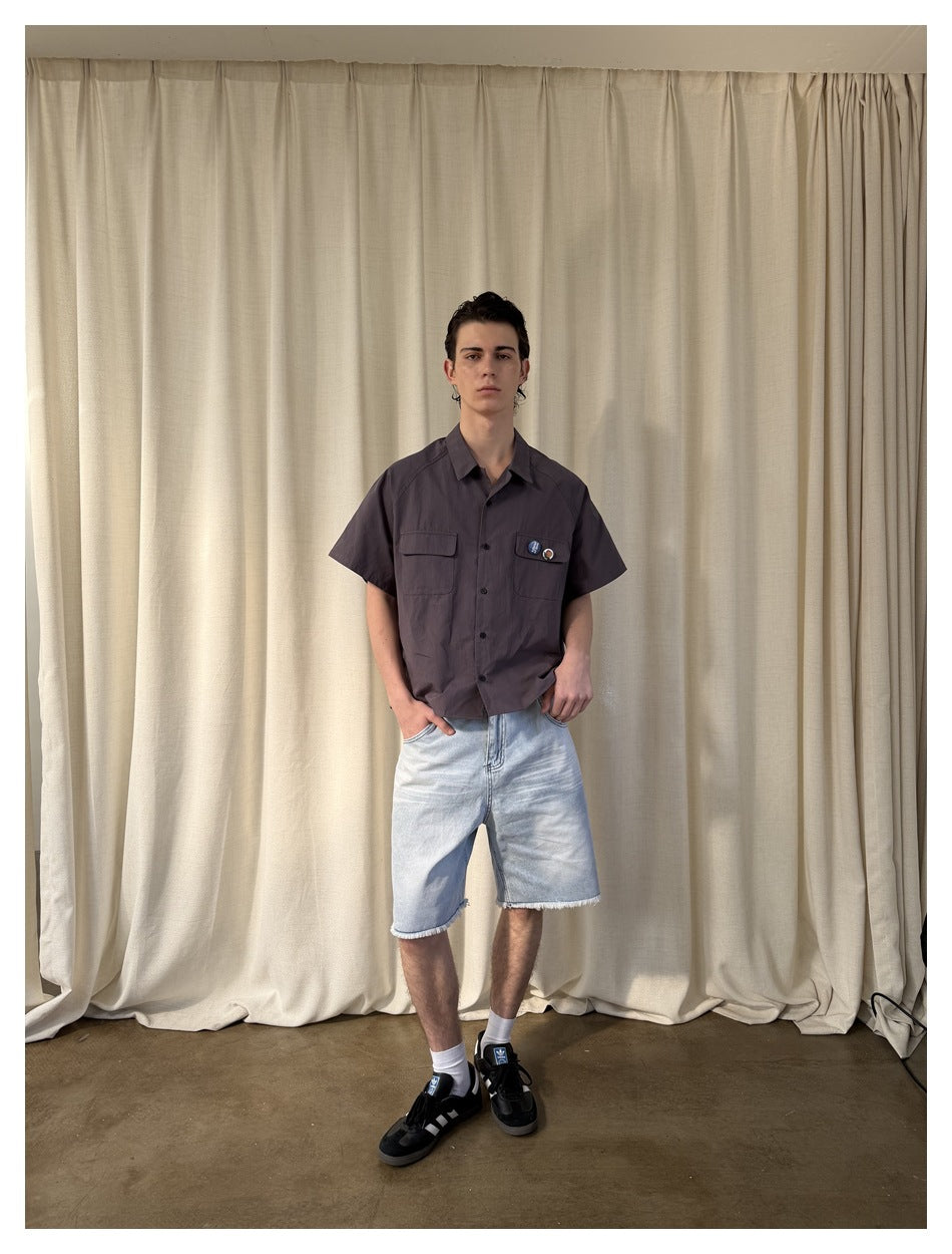 Full-length front view of a model wearing a charcoal two-pocket button-up shirt and light-wash denim shorts.