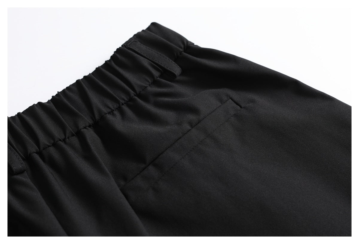 Close-up of black trousers showing a gathered waistband, belt loop, and slanted front pocket.