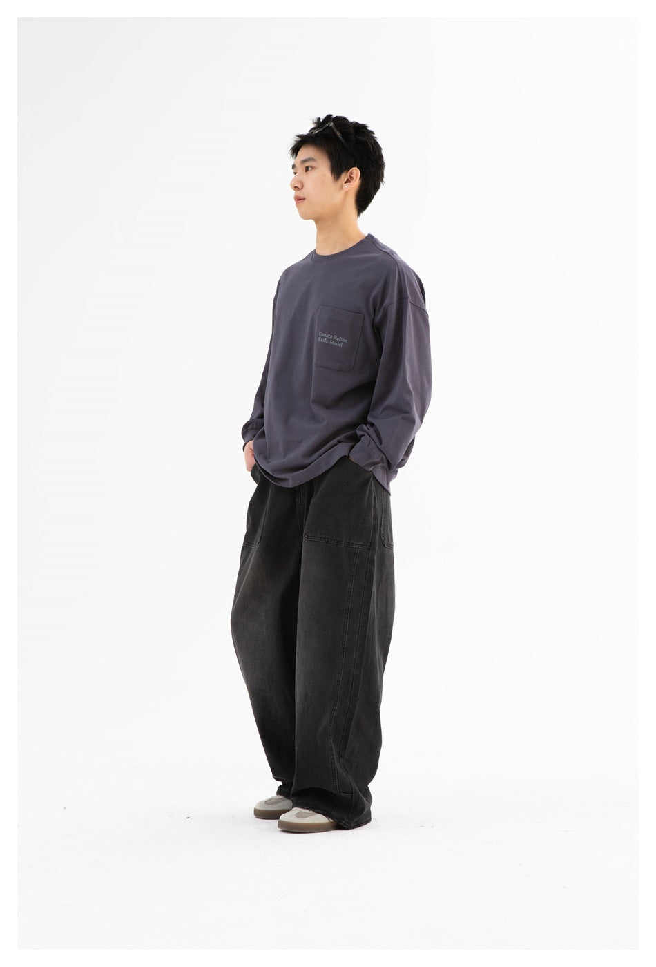 Full-length three-quarter view of a model wearing a charcoal-gray pocket sweatshirt and loose black pants.
